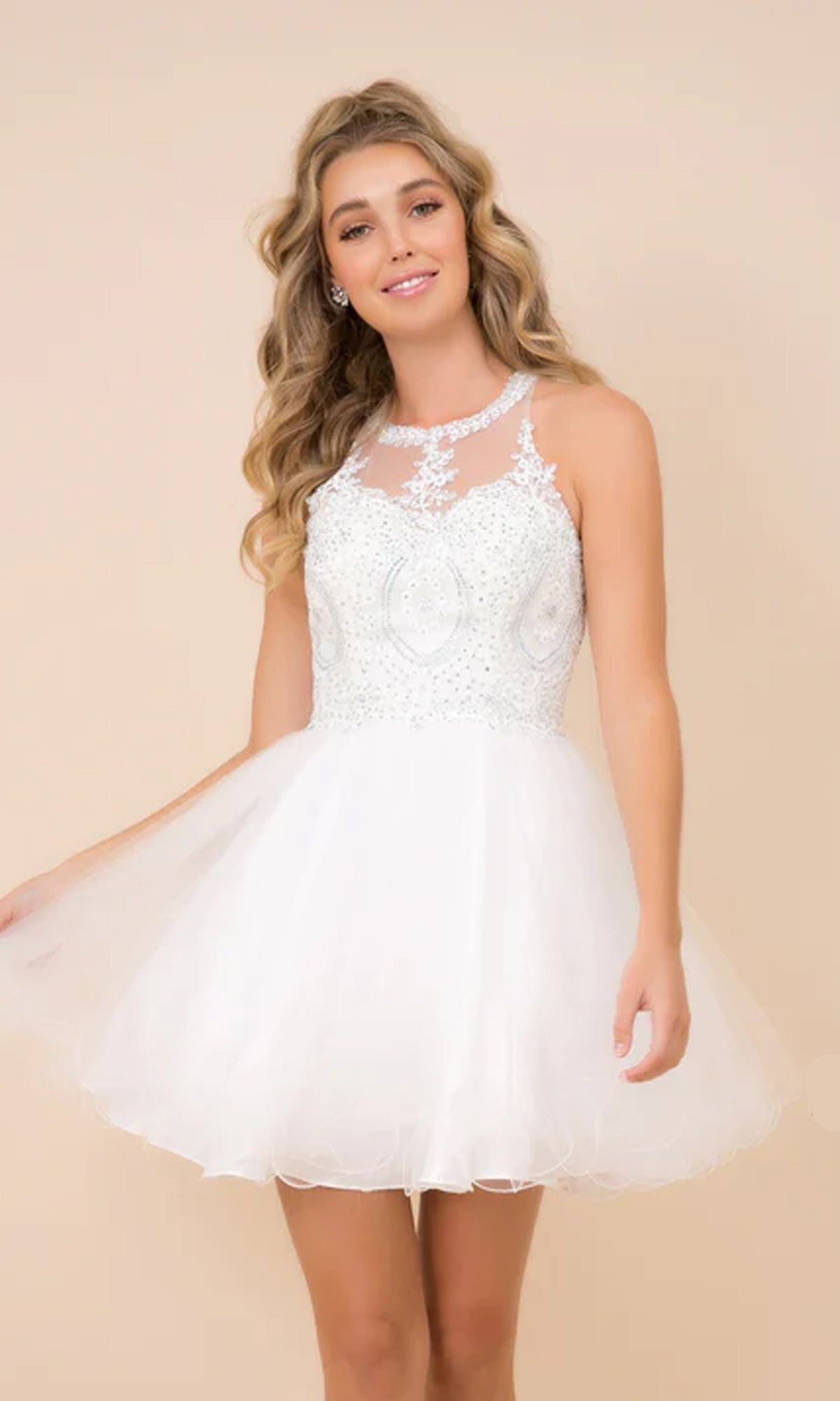A young woman poses against a beige background in a Short Babydoll Homecoming Dress with Beading, featuring a sheer embellished bodice and flared tulle skirt.